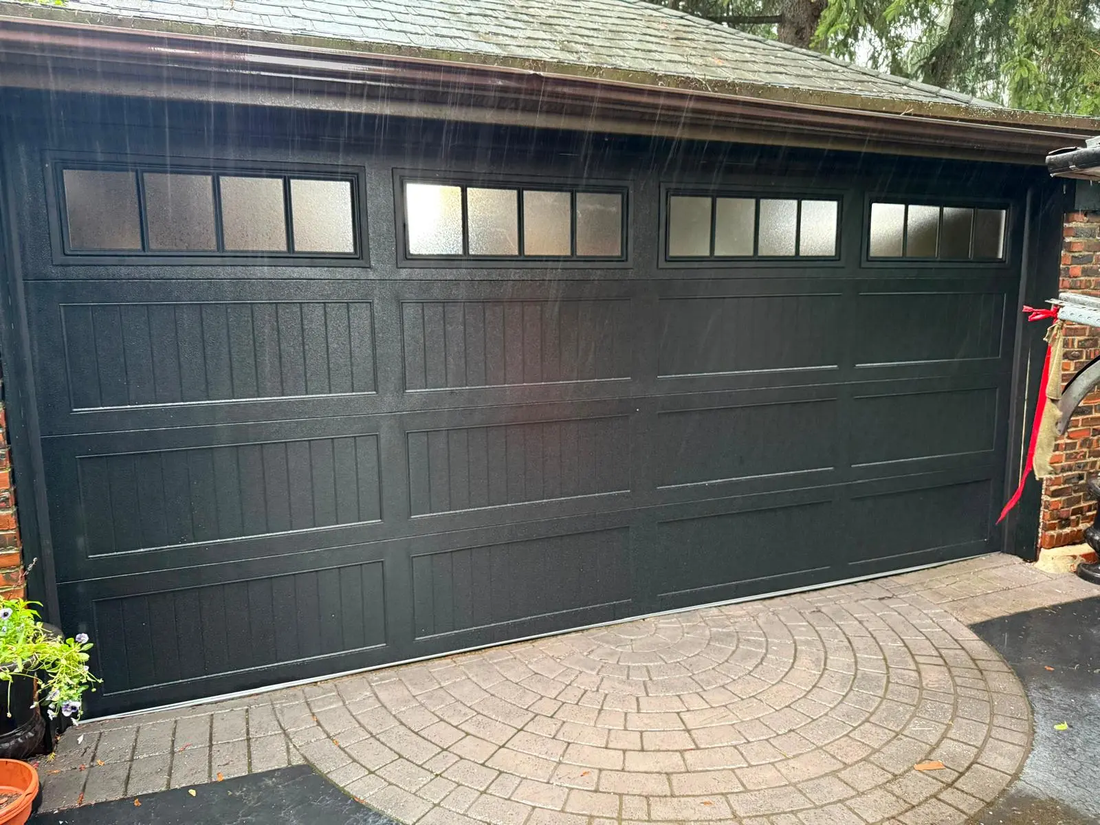 Black double-car garage door with frosted windows on a paver driveway